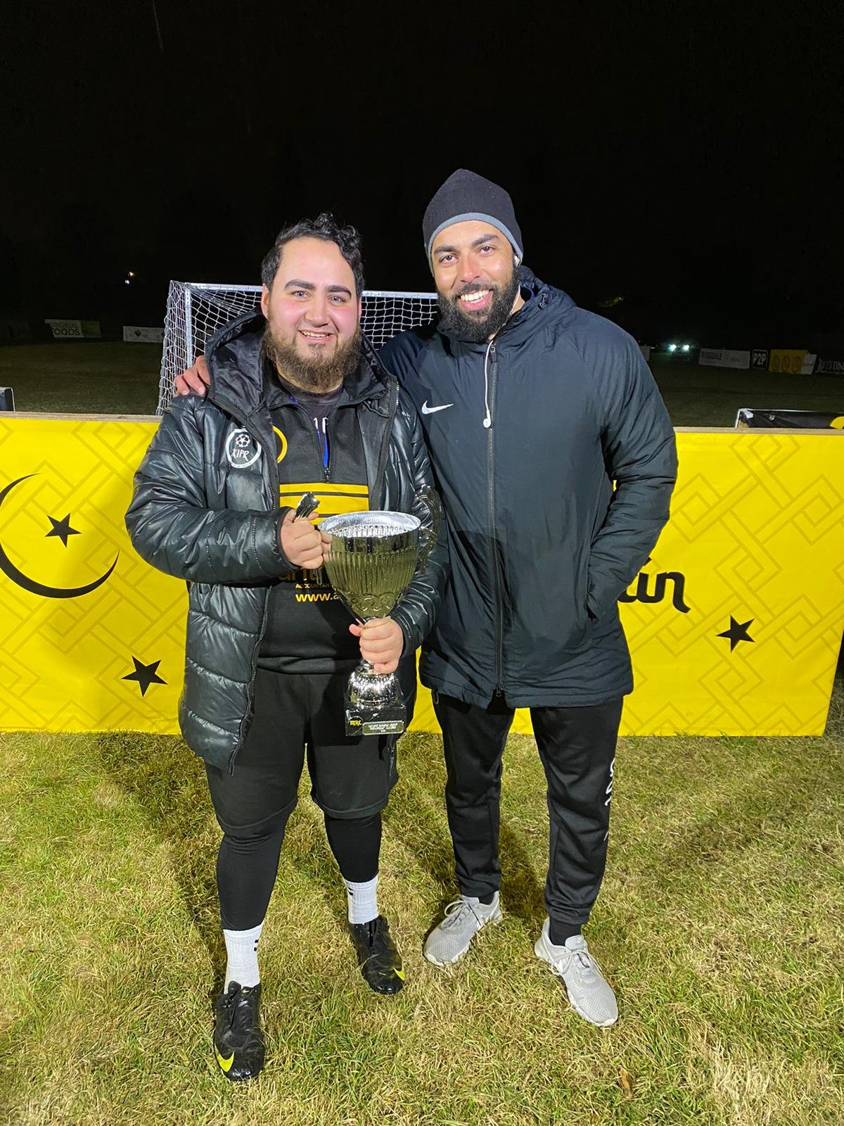 Huzefa Vorajee holding a cup trophy with a teammate after a non-league final